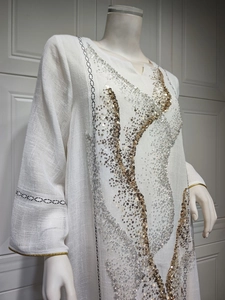 Detail view of a white linen-style dress with gold and silver sequins and embroidery