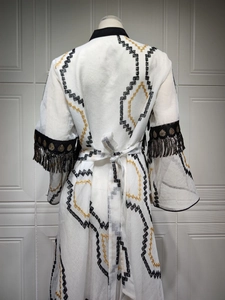 Detailed embroidery on white long-sleeve robe with gold sequins and black tassels