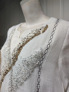 Close-up detail of white linen dress featuring gold and silver sequins and embroidery.