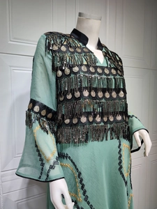 Detail of mint green evening dress featuring black fringe tassels and gold sequins