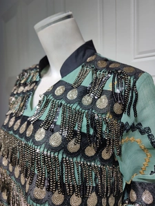 Detail of teal sequin embroidery with black fringe tassels on a high collar evening dress