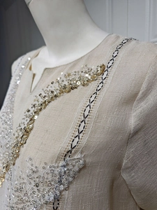 Close-up of elegant sequin embroidery and textured fabric on a beige summer pullover dress.