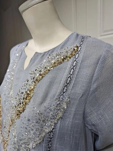Detailed close-up of light blue linen dress with gold sequins and black embroidery detail