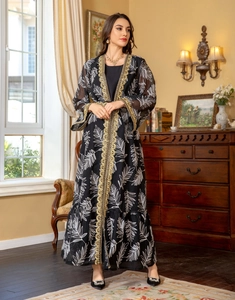Detail of black kaftan with white leaf patterns and gold embroidery in elegant setting