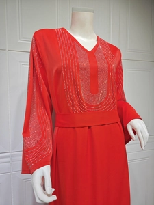 Détail des motifs en strass argentés sur le décolleté d'une robe caftan rouge