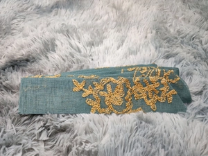Detailed close-up of golden floral embroidery on blue-grey ethnic fabric belt accessory