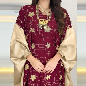 Detail of burgundy kaftan with intricate gold floral embroidery and tassel necklace