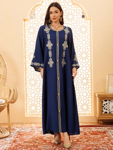 Détail de la broderie géométrique dorée sur la manche d'une robe longue bleu marine ethnique