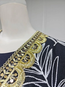 Close-up of ethnic embroidery with gold lace trim and sequins on navy mesh fabric