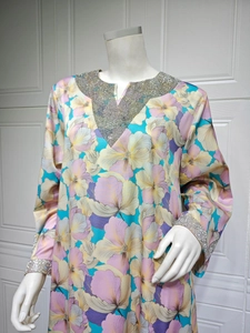 Détail de l'encolure en V d'une robe longue fleurie avec bordure en strass argentés et manches