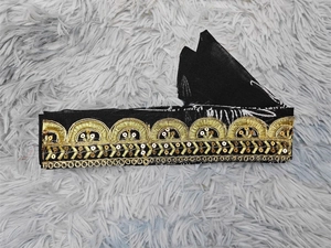 Detail of black mesh ribbon with ethnic gold embroidery and sequins on gray background