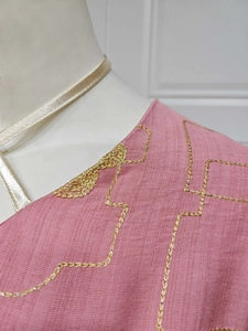 Close-up of pink fabric with gold geometric embroidery and textured material details
