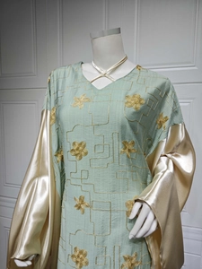Detail of mint green caftan dress featuring gold floral embroidery and champagne satin sleeves