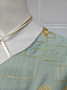 Close-up of mint green textured fabric with intricate gold embroidery and champagne tie