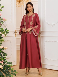 Détails de broderies dorées sur une robe caftan bordeaux dans un décor intérieur luxueux