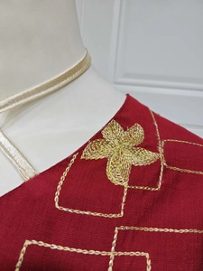 Detail of red dress neckline featuring intricate gold floral embroidery and silky fabric