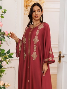Détail de la broderie dorée complexe sur l'encolure et les poignets d'une robe rouge ethnique