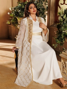 Detail eines weißen Maxikleids mit goldener geometrischer Stickerei und transparentem Cardigan