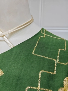 Close-up of dark green linen dress featuring gold chain embroidery and ivory satin neck tie