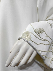 Macro detail of silk satin sleeve with gold and silver floral embroidery on white dress