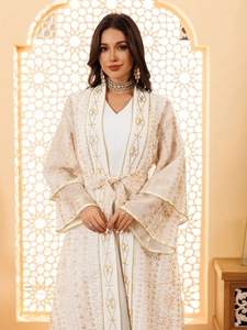 Détail de robe en tulle blanc avec broderies géométriques dorées et manches évasées