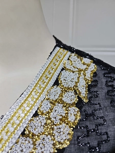 Detailansicht der aufwendigen gold-weißen Perlenstickerei auf schwarzem Netzkleid