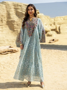 Detailed embroidery on light blue kaftan dress against a desert landscape background