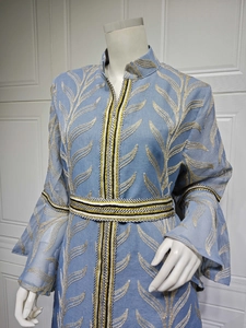 Detailed close-up of golden embroidery and woven decorative tape on light blue kaftan dress