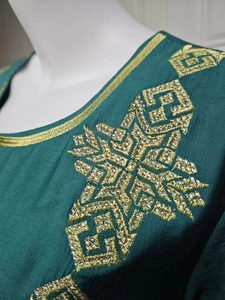 Vue macro des broderies dorées et paillettes argentées sur la robe ethnique verte