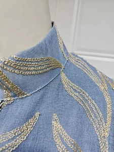 Close-up of wavy gold embroidery on the high collar of a light blue linen midi dress