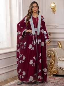 Détail de broderies florales argentées et pompons sur une robe caftan bordeaux