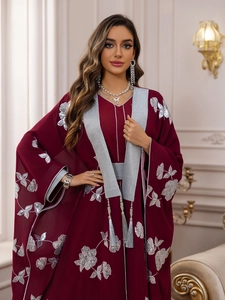 Détails de broderies florales argentées et glands sur une robe caftan bordeaux
