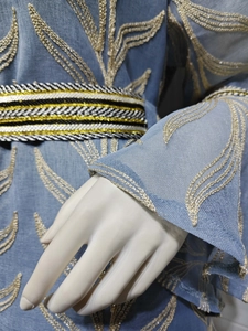 Close-up of golden leaf embroidery and textured blue fabric with a braided belt detail