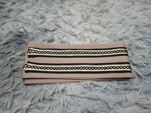 Detail eines khakifarbenen Stickgürtels mit schwarz-goldenen Flechtmustern im Zickzack