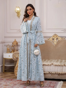 Dettaglio dell'abaya ricamata azzurra con bordo in paillettes dorate e motivi floreali bianchi