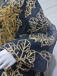 Detailed view of luxury gold embroidery and sequined leaf patterns on a black kaftan dress