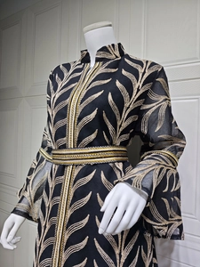 Close-up of golden leaf embroidery and geometric woven belt on black kaftan dress