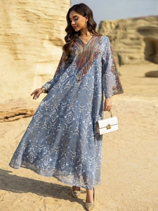 Détails de broderie et pompons sur robe longue ethnique bleue dans un décor de désert