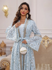 Dettaglio di abaya ricamata azzurra con motivi floreali bianchi e bordi in paillettes