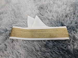 Détails de la broderie dorée et du motif tissé sur cet accessoire de tête blanc