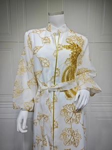Detailed close-up of golden sequin leaf embroidery and intricate beadwork on white dress