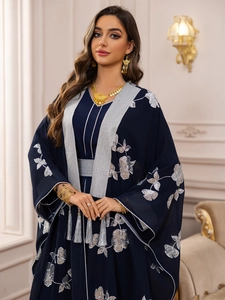 Détail de robe brodée bleu marine avec motifs floraux argentés et longues franges de glands