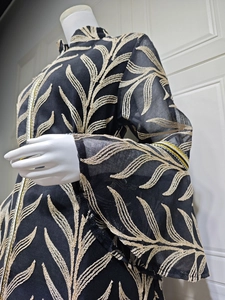 Detail of gold leaf embroidery and flared sleeves on elegant black mesh evening dress