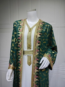 Détails du caftan vert avec motifs de plumes dorées et glands perlés sur l'ourlet