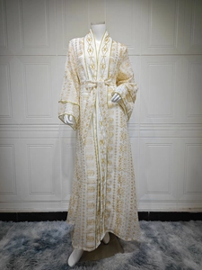 Détail de broderie dorée sur robe abaya blanche en mesh avec motifs floraux complexes