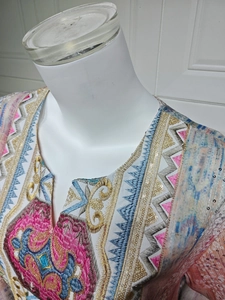 Détail du col en V ethnique avec broderies colorées et paillettes dorées sur la robe