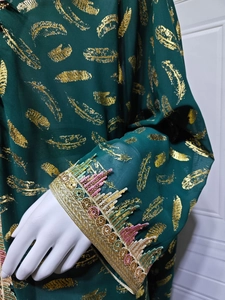 Détail de la manche en mousseline vert foncé avec plumes dorées et broderie de sequins