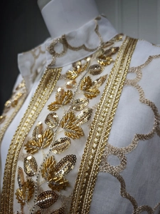 Detailaufnahme der aufwendigen goldenen Paillettenstickerei auf weißem Organza-Cardigan