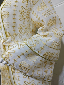 Détail d'une robe en tulle blanc avec broderie géométrique dorée et manches larges