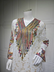 Détail de la broderie à paillettes colorées sur le col en V d'une robe caftan blanche en tulle